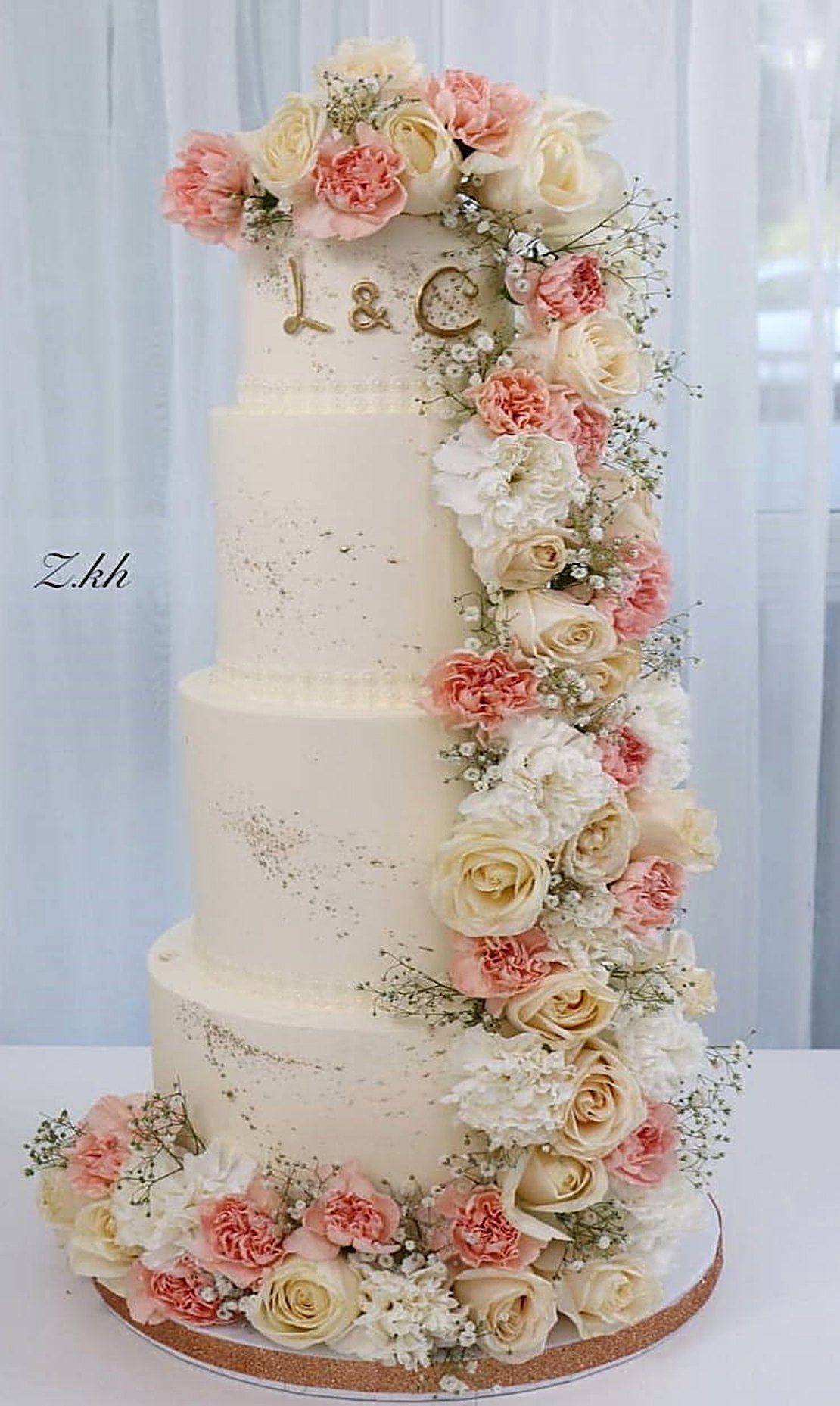 Four-tier wedding cake with a cascade of peach and cream roses, initials L & C